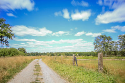 Dirt road amidst field against sky