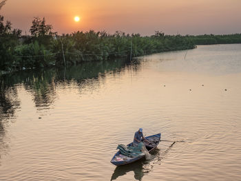 Person on boat in lake against sky during sunset