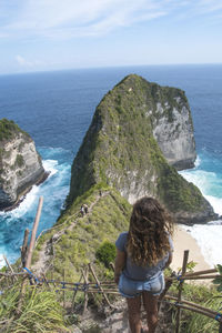 Rear view of woman standing on cliff against sea