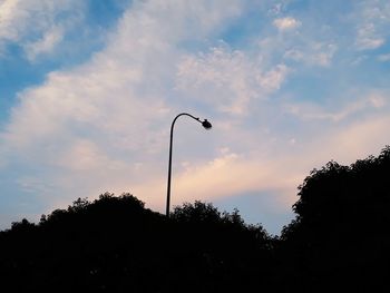 Low angle view of silhouette bird perching on street light against sky