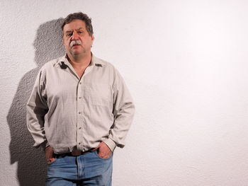 Portrait of man with hands in pocket standing against wall