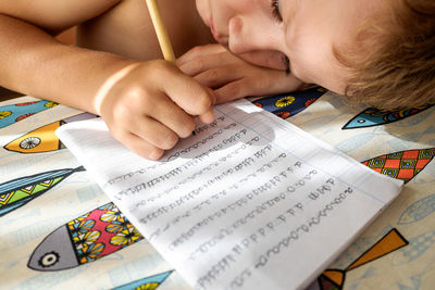 High angle view of cute boy writing in book on table