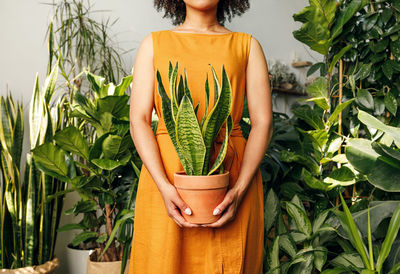 Midsection of teenage girl holding potted plant amid plants