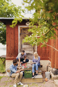 Friends eating watermelon and having drink while sitting outside cottage