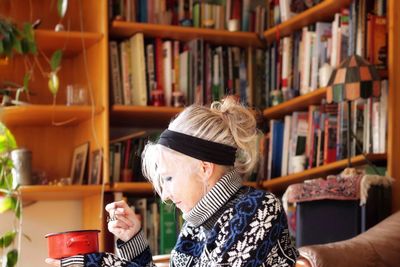 Senior woman sitting against book shelf at home