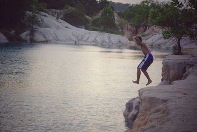 Side view of young man jumping in lake during sunset