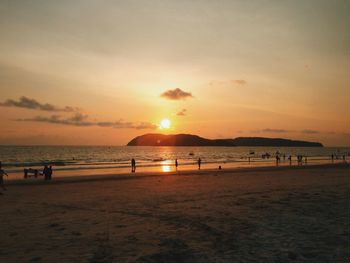 Silhouette people enjoying on sea shore against sky during sunset