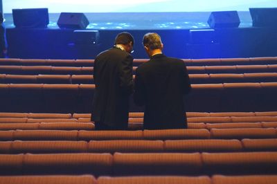 Rear view of business people standing amidst bleachers in theater