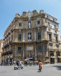 People riding bicycle on road against buildings