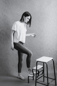 Portrait of young woman standing on chair against wall