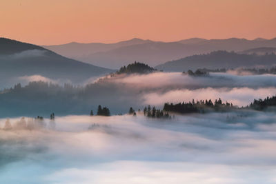 Scenic view of fog covered mountains against sky during sunrise