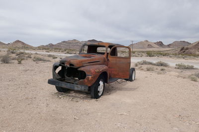 Abandoned car on desert against sky