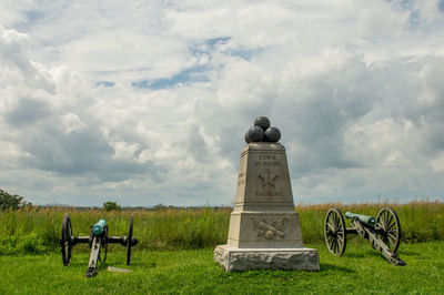 Historical monument and cannons on field against cloudy sky