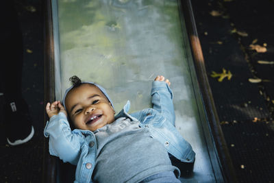 High angle portrait of happy cute baby girl sliding at playground