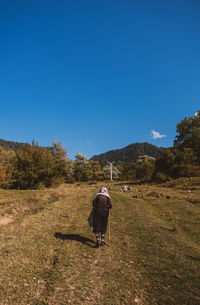 Rear view of man walking on field against clear sky