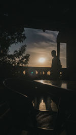 Silhouette man sitting by car against sky during sunset