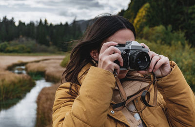 Portrait of young woman taking photos of beautiful autumn nature with a vintage film