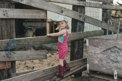 A young girl stands on a fence wearing a leotard and cowgirl boots.