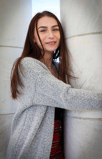 Portrait of smiling young woman against wall