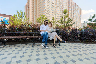 Full length smiling couple sitting on park bench