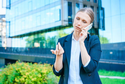 Successful female banker using smart phone outdoors while standing near office