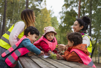 Preschool teachers and students eating grapes outdoors