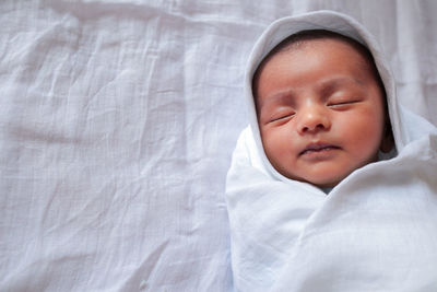 High angle view of baby boy wrapped in blanket sleeping on bed