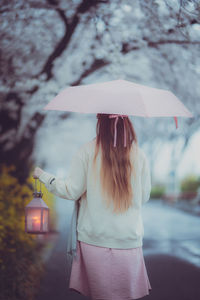 Rear view of woman with umbrella standing in rain