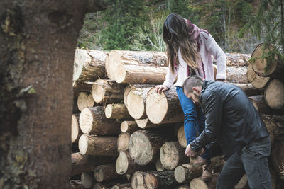 Young man tying shoelace of girlfriend against logs of wood 