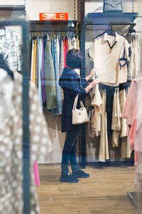 A 40-year-old brunette woman in a blue jacket is choosing clothes in a store.