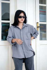 Portrait of young woman wearing sunglasses while standing against wall