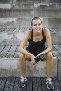 Portrait of smiling woman holding water bottle while sitting on steps