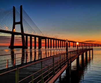 Bridge over tagus river against sky with a beautiful sunrise from a pier at nations park lisbon