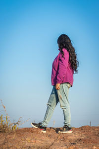 Isolated young girl standing at mountain top with blue sky from flat angle