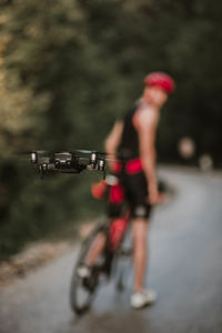 Close-up of drone flying while man with bicycle standing on road