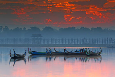 Boats moored in lake against sky during sunset