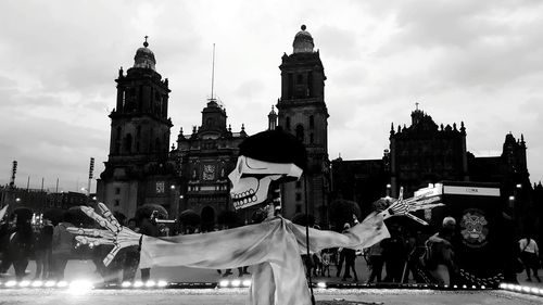 Statue of buildings in city against cloudy sky