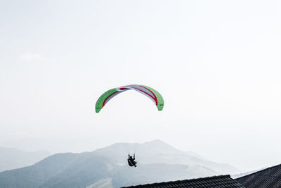 Person paragliding over mountain against sky