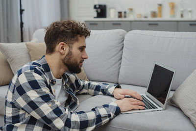 Young man using laptop while sitting on bed at home