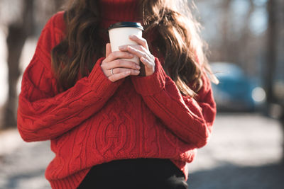 Pregnant woman holding paper cup of coffee take away outdoors. wearing red knitted sweater closeup