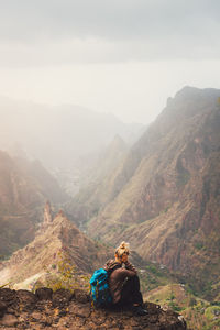 Rear view of woman sitting on cliff against sky