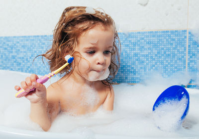 Cute girl holding toothbrush while sitting in bathtub