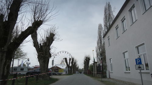 Road amidst bare trees against sky in city