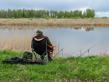 Rear view of man sitting on field by lake