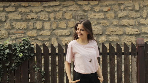 Portrait of smiling young woman standing against brick wall