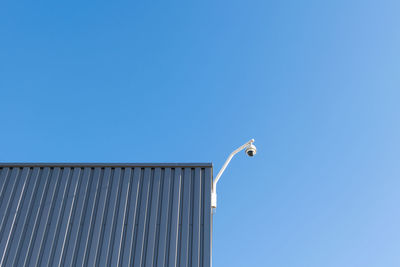 Low angle view of security camera against clear blue sky