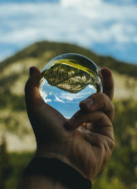 Close-up of hand holding crystal ball against mountain