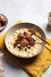 High angle of bowl with tasty milk oatmeal served with crunchy chocolate balls pumpkin seeds and pecan nut on napkin for healthy breakfast