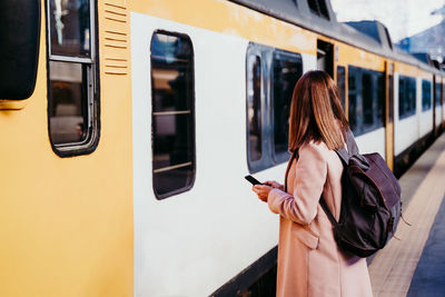 Woman with phone standing by train on railroad station platform