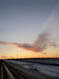 Road by field against sky during sunset